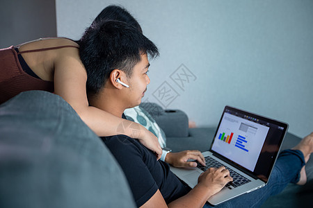 亚洲年轻微笑夫妇拥抱和使用无线耳机 并使用在家工作的电脑笔记本 他正在为家里的在线会议准备图表和信息女朋友女孩男性房间夫妻男人女图片