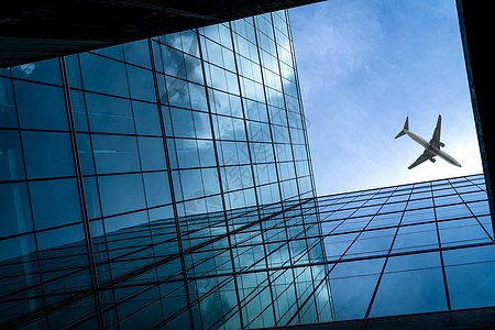 飞机在现代玻璃办公大楼上空飞行 透视图片