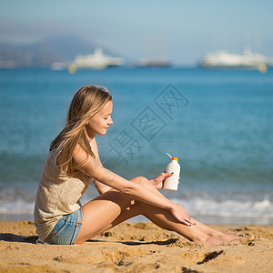 年轻妇女在腿上涂防晒霜防晒润肤紫外线管子太阳推杆皮肤天空日光浴晴天图片