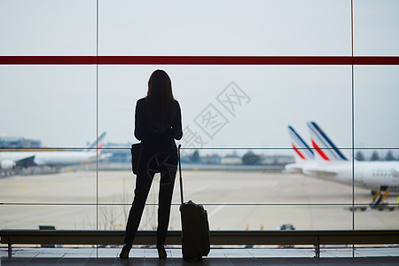 携带手提行李的女士在国际机场寻找长途旅行者服务员人员玻璃航班套装航空公司旅行全体飞机背光图片