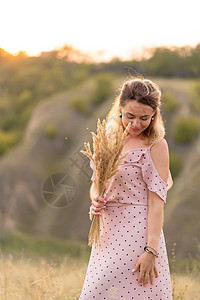 穿着白外衣的美丽年轻女孩 在日落时走在田地里 带了根花束荒野乐趣小麦太阳微笑文化收成村庄女性裙子图片