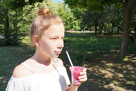在阳光明媚的一天 女孩在公园里拿着一根稻草喝着水果鸡尾酒休闲青少年玻璃液体稻草活动果汁热带橙子饮料图片