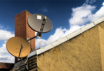 两台卫星天盘 在一栋房屋屋顶上一个红砖烟囱前图片
