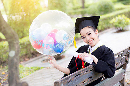 穿着学术服和学校服装的年轻快乐女毕业生肖像学习成人微笑证书女士研究生仪式气球文凭长袍图片