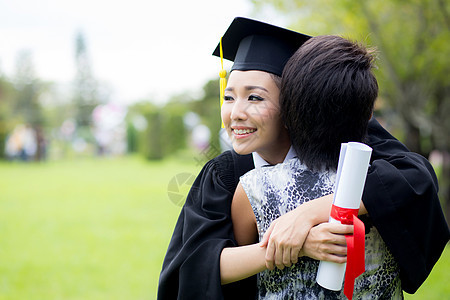 年轻女毕业生在毕业典礼上拥抱她朋友的抱抱成功女士微笑学生家庭女性帽子教育学校校园图片