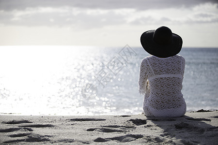 坐在海边留着长发的年轻女子在黎明时分在风中看着地平线 身着白色蕾丝连衣裙 白色内衣和大黑帽海景帽子女性天空戏剧性孤独悲伤身体生活图片