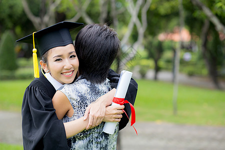 年轻女毕业生在毕业典礼上拥抱她朋友的抱抱文凭女孩微笑女性校园母亲成功大学教育家庭图片
