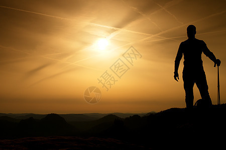 手握有杆子的旅游者站在岩石上观望下一步男生男人射线自由薄雾太阳阴影姿势伙伴游客图片