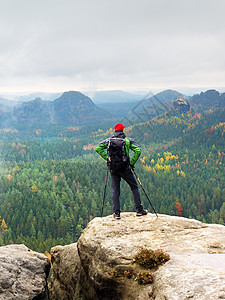 顶顶上带手边有杆和重型背包的旅游导游 红帽远足男生顶峰男人旅行夹克呼吸阴影自由岩石图片