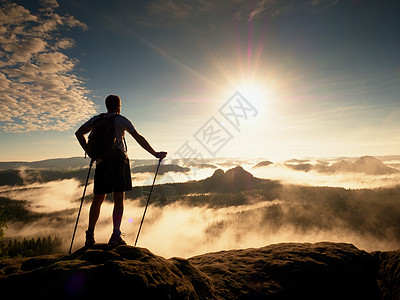 高高的背包手持电杆 在岩石山上阳光薄雾图片