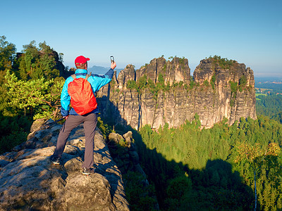 有红色背包的旅游者 带着岩石和山谷的手机拍照图片
