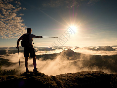 高高的背包机手握有杆子 在岩石山上阳光明媚的日出冒险山顶活动运动旅行者薄雾背包自由休息游客图片
