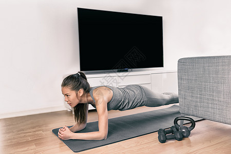 在家里进行健身锻炼 亚洲女孩做木板练习以锻炼核心观看健身课的电视视频 不去健身房就在电视机前训练肌肉的年轻女性活动力量沙发公寓地图片