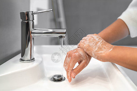 手洗泡沫肥皂揉手腕洗手步女人在浴室水龙头水槽的水中冲洗 洗手以预防 COVID-19 传播 冠状病毒大流行爆发图片