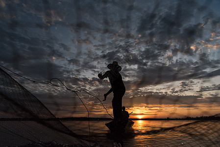 渔民在W日落时扔鱼网钓鱼的休光灯橙子生活渔夫蓝色太阳瓦农男人天空图片