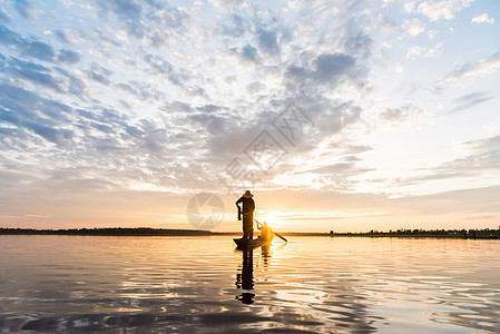 渔民在W日落时扔鱼网钓鱼的休光灯天空渔夫橙子瓦农太阳蓝色生活男人图片