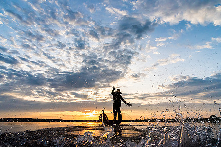 渔民在W日落时扔鱼网钓鱼的休光灯蓝色渔夫男人瓦农天空橙子太阳生活图片