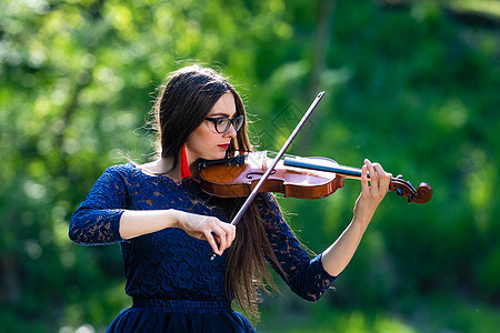 在公园玩小提琴的年轻女子 浅浅的田野树木音乐会女孩头发旋律玩家音乐家细绳娱乐情感图片