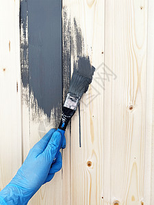 穿蓝橡胶手套的工人用灰色油漆刷着一堵木墙 修整表面装潢师画家乡村工作刷子右手画笔房子涂层木头图片