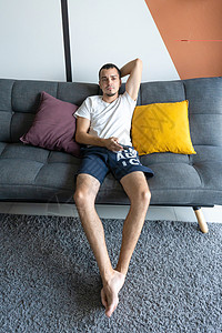 一个穿家庭服装的瘦子坐在沙发上看电视 无聊透顶控制程序丈夫白色房间手表闲暇控制板男人男性图片