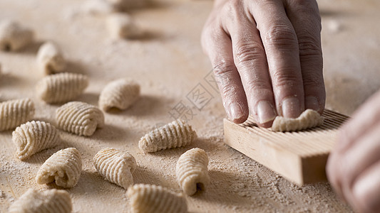 用全麦面粉制作自制素食意大利面的特写过程 家庭厨师在特殊的木制工具上爬行 gnocco 传统的意大利面食 女人在厨房里做饭饺子糖图片