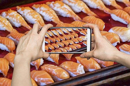 女孩在手机智能手机上拍照 在摊间吃寿司图片