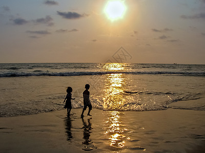 Sillhoute的画面 男孩和一个女孩在海上玩耍 在美丽的日落的背景图片