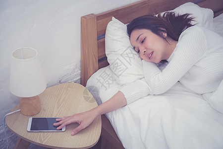 熟睡妇女的手在手机上用闹钟唤醒技术电话警报假期女性苏醒卧室桌子睡眠时间图片