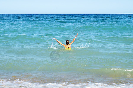 在海中举起双手的女孩 在后视线下天空女性海滩快乐行动海洋女士乐趣飞溅海浪图片
