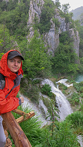 在普利维茨湖泊国家公园背景瀑布中 一个穿红色夹克的青少年站在瀑布上站立着一排小矮人图片