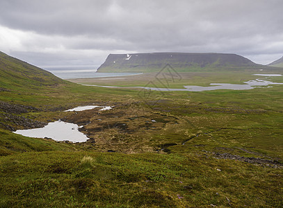 北部夏季景观 在冰岛西部峡湾自然保护区的 adalvik 湾美丽的悬崖上欣赏河流三角洲 沙滩和大海 积雪覆盖的绿色草地和乌云背景图片