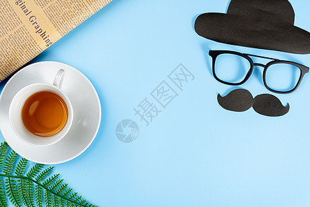 父亲节快乐背景概念 带眼镜 黑胡子 帽子 报纸 叶子和蓝色背景的茶杯 带有文本复制空间图片