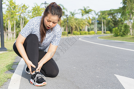 亚裔女性在路上时用手抓住脚踝肌腱按摩痛苦肌肉训练伤害疼痛赛跑者膝盖阳光图片