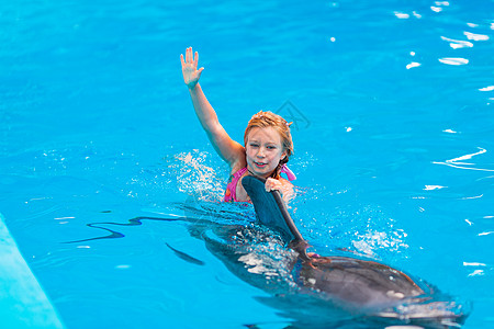 快乐的小女孩与海豚在海豚馆游泳治疗潜水荒野野生动物拥抱蓝色海洋水池宠物朋友图片
