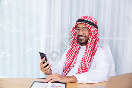 阿拉伯商务人士笑笑并快乐地阅读他的喜讯办公室电话工程师手机商业职业工作微笑建筑学经理背景图片
