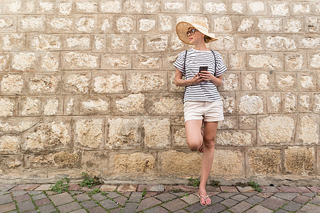 美丽的年轻旅游女青年站在旧的地中海城镇古板石墙前 微笑 握持 智能电话在度假时网络上进行交流 复制空间Ryp space楼梯石头图片