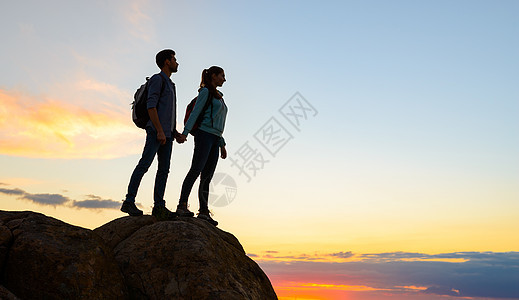 青年旅游者在夏季日落时站在岩石顶端 家庭旅行和冒险概念组织首脑远足伙伴团队帮助女士阳光友谊悬崖男人图片