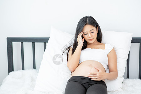 美丽的亚洲孕妇展示出精神紧张和头痛的动作 她们躺在床上 晨光照亮女性女士母亲压力怀孕肚子压抑沮丧情感疾病图片