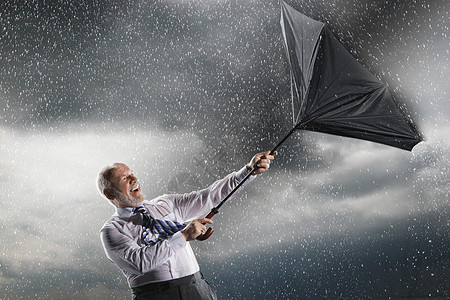 商务人士在暴风雨中拼命地抓住内外伞图片