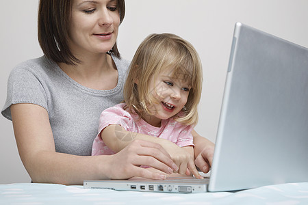 在家用笔记本电脑在桌子上工作的妇女 而婴儿则坐在她女儿的旁边孩子黑发父母互联网技术自由职业者女性母性女士妈妈图片
