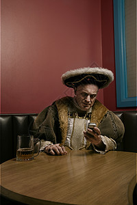 亨利八世国王在餐桌上使用移动电话桌子困惑啤酒财富版税收腰手机沟通饮料古装图片