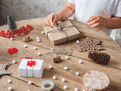 孩子把圣诞礼物包装在手纸上 白毛卷白色乡村手工盒子儿童新年红色绒球边缘丝带工艺图片