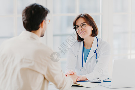 自信的女医生握着病人的手 说服一切都会好起来的 穿着白色的医用长袍 提出建议 在医院办公室摆姿势 咨询和诊断概念图片