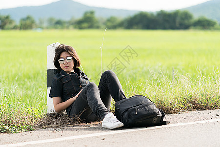 女人坐着背包搭便车在路上女士女孩太阳镜场地自由天空短发游客行李成人图片