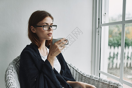 戴眼镜的漂亮女人坐在窗户旁边 喝着一杯咖啡图片