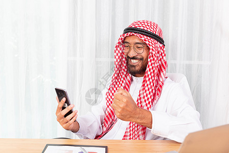 阿拉伯商务人士笑笑并快乐地阅读他的喜讯技术职业交易建筑师电话经理建造建筑学帽子商业背景图片