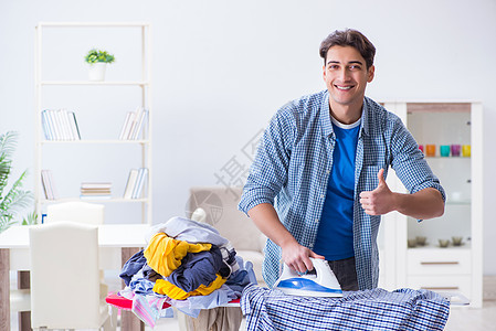 年轻男子丈夫在家穿衣服熨衣服家政服务打扫熨烫房间家庭帮助外包洗衣店工人图片