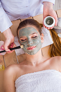 带面罩的女青年在温泉保健概念中按摩皮肤刷子保湿呵护蜡烛黏土女士女孩化妆品图片