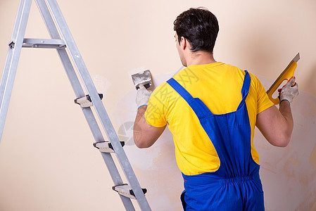 在墙上涂石膏的年轻承包商雇员水泥维修劳动者建筑工人石膏板工匠梯子画家装修图片