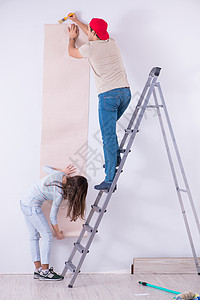 年轻家庭在家里用新墙纸翻新家房团队公寓工人妻子男人女士改造维修建筑梯子图片